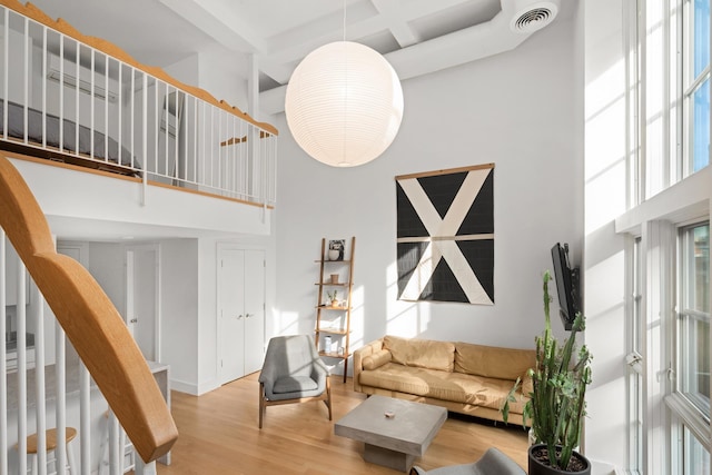 living area featuring visible vents, beamed ceiling, coffered ceiling, light wood finished floors, and a towering ceiling