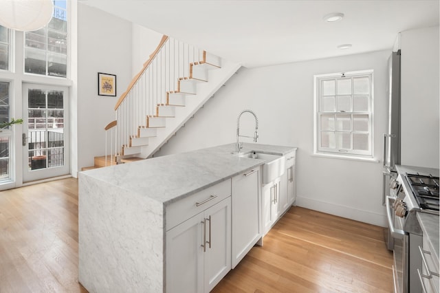 kitchen featuring light wood-style flooring, light stone countertops, stainless steel gas range, and a sink