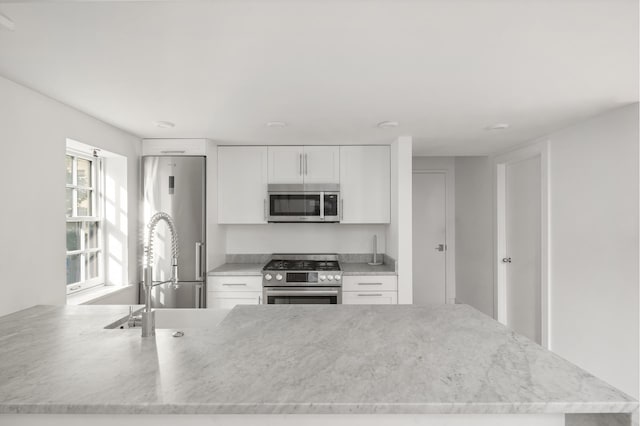 kitchen with stainless steel appliances, white cabinetry, and light stone counters