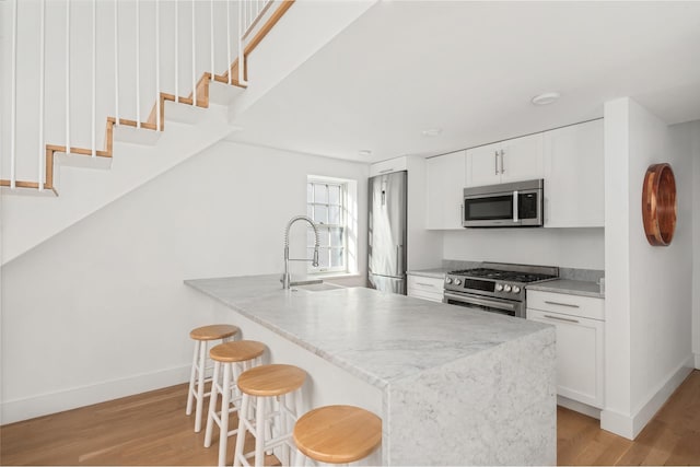 kitchen with light wood-type flooring, a breakfast bar, a sink, appliances with stainless steel finishes, and white cabinets