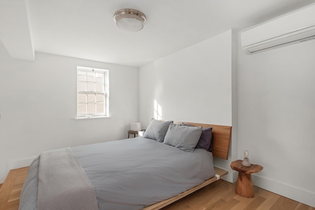 bedroom with baseboards, an AC wall unit, and wood finished floors