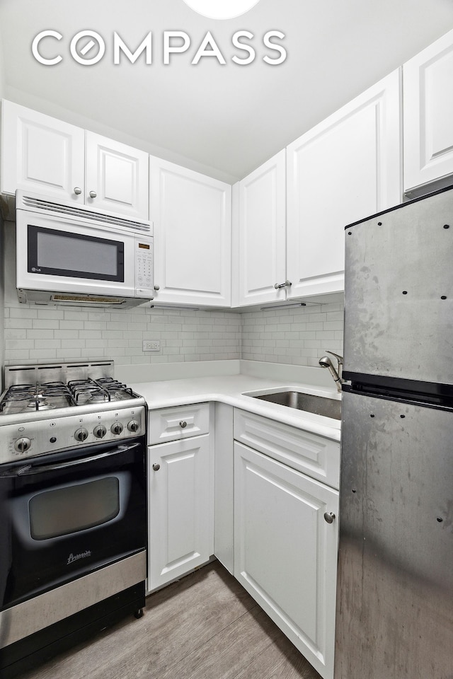 kitchen with decorative backsplash, appliances with stainless steel finishes, light wood-style floors, and a sink