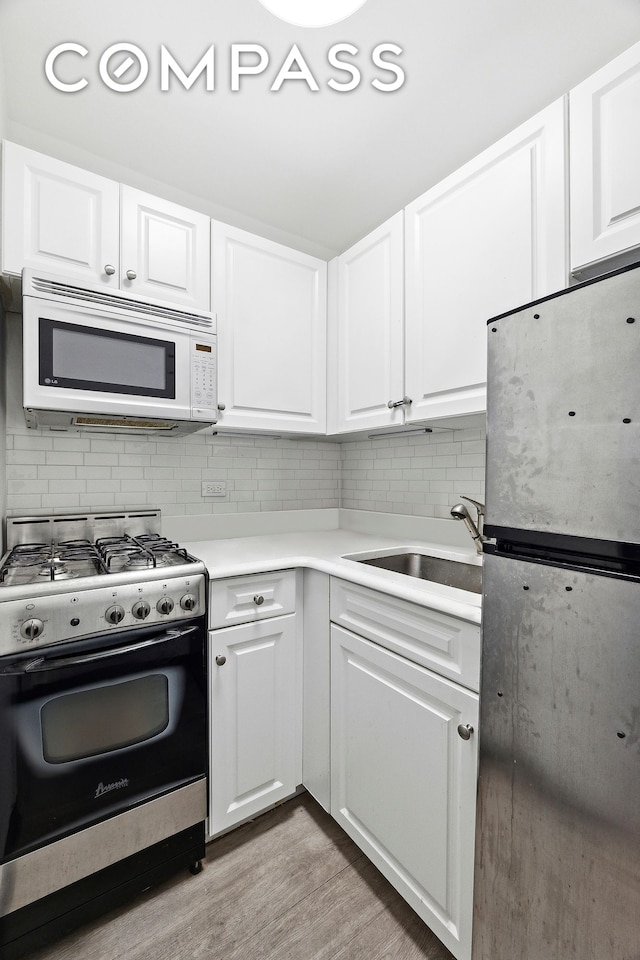 kitchen with decorative backsplash, appliances with stainless steel finishes, light wood-type flooring, a sink, and white cabinetry