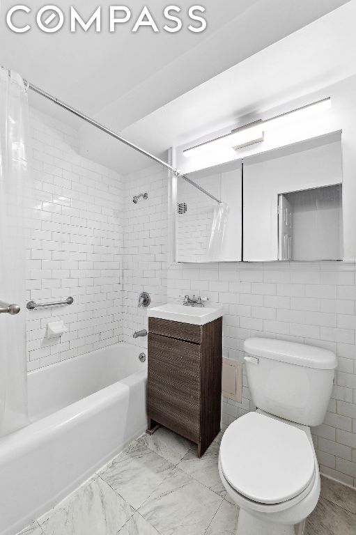 full bathroom featuring toilet, tiled shower / bath combo, tile walls, and vanity