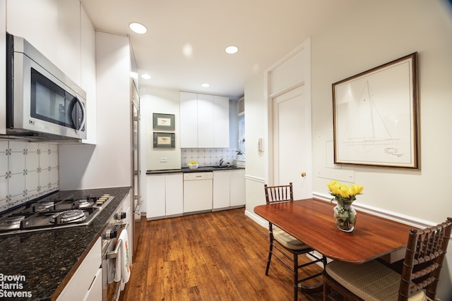 kitchen with appliances with stainless steel finishes, sink, white cabinets, tasteful backsplash, and dark wood-type flooring