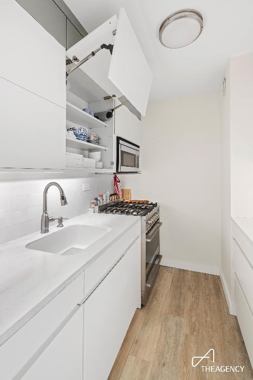 kitchen featuring appliances with stainless steel finishes, sink, backsplash, white cabinetry, and light hardwood / wood-style floors