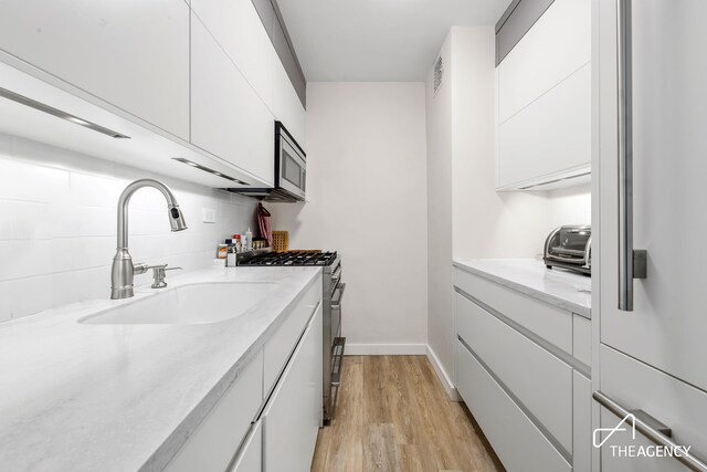 kitchen featuring light hardwood / wood-style flooring, sink, tasteful backsplash, white cabinetry, and stainless steel appliances