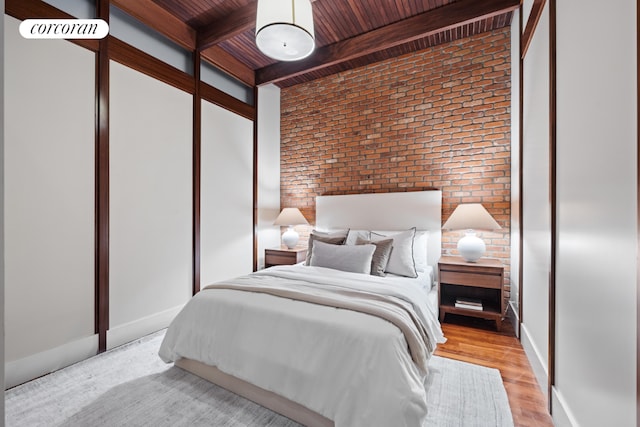 bedroom with beamed ceiling, brick wall, light wood-type flooring, and wood ceiling