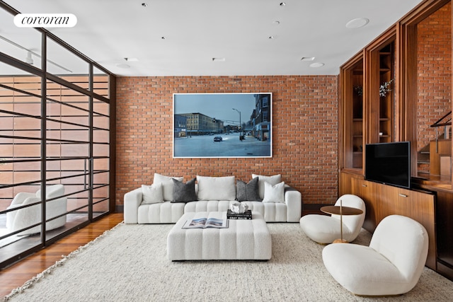 living room featuring wood-type flooring, expansive windows, and brick wall