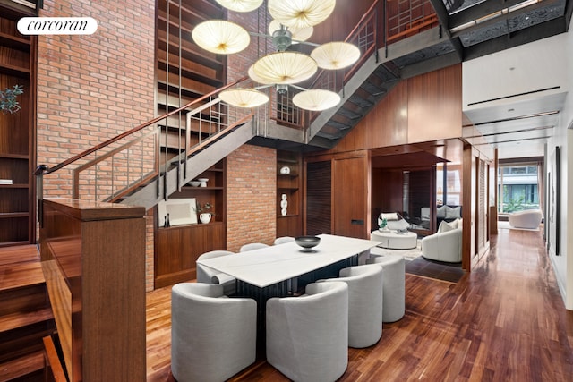 dining space with brick wall, wood walls, dark hardwood / wood-style flooring, a high ceiling, and built in shelves