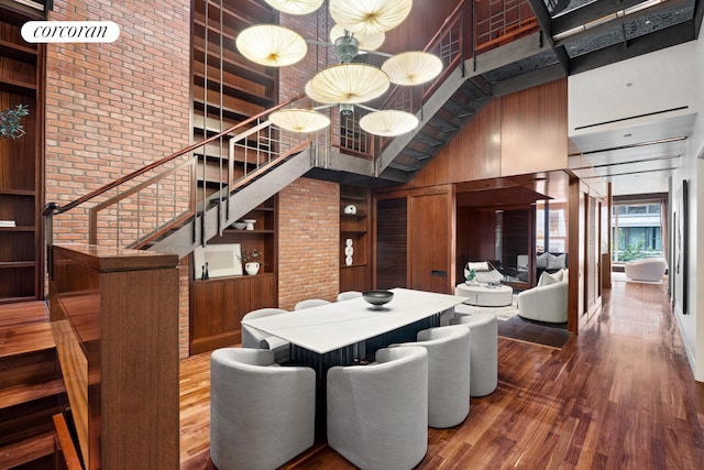 dining room featuring stairway, wooden walls, built in features, wood finished floors, and a towering ceiling