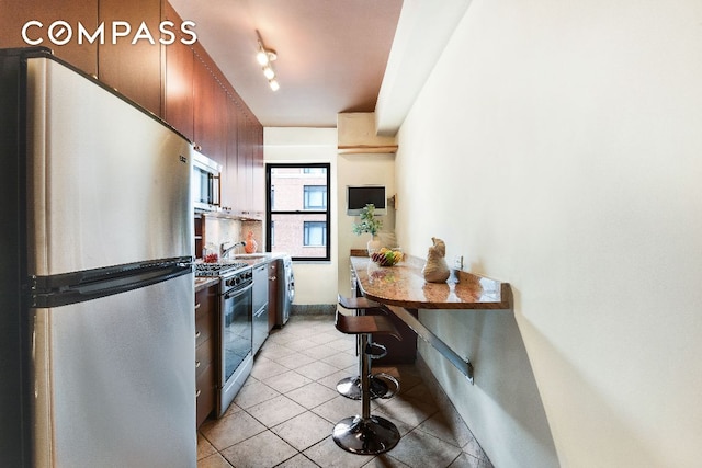 kitchen featuring light tile patterned flooring, sink, track lighting, appliances with stainless steel finishes, and backsplash