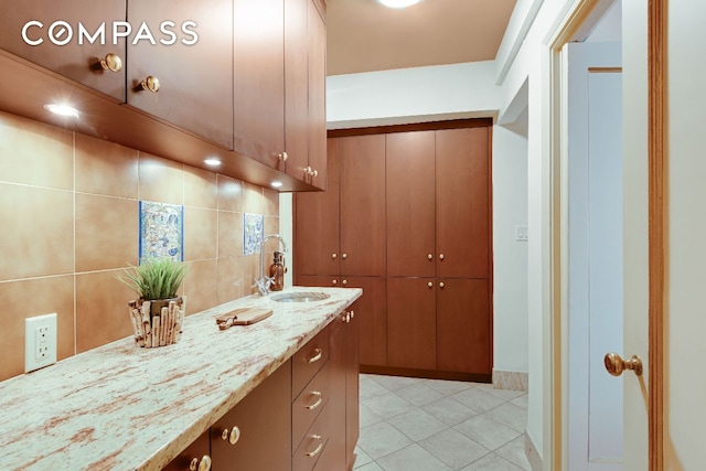 interior space featuring light tile patterned flooring, sink, light stone counters, and decorative backsplash