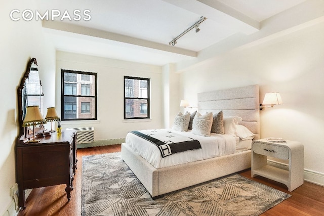 bedroom with track lighting, beam ceiling, hardwood / wood-style floors, and a wall unit AC