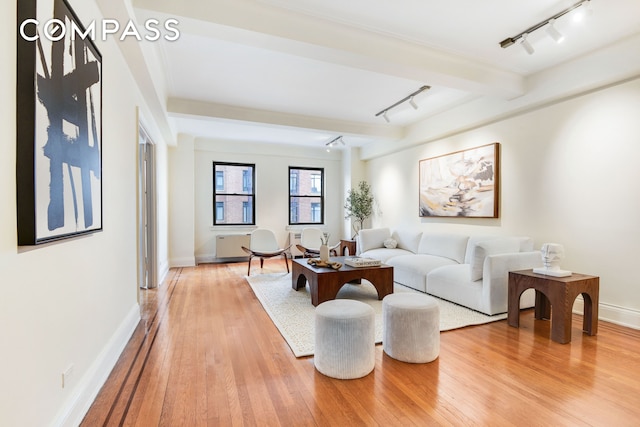 living room featuring beamed ceiling, rail lighting, light wood-style flooring, and baseboards