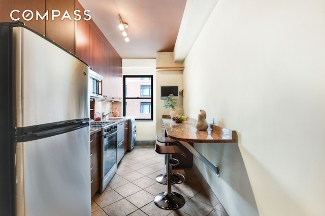 kitchen with appliances with stainless steel finishes, light tile patterned flooring, a sink, and tasteful backsplash