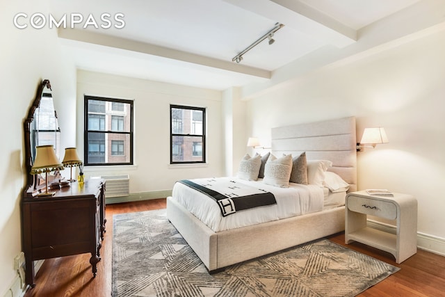 bedroom featuring rail lighting, a wall mounted AC, wood finished floors, beamed ceiling, and baseboards