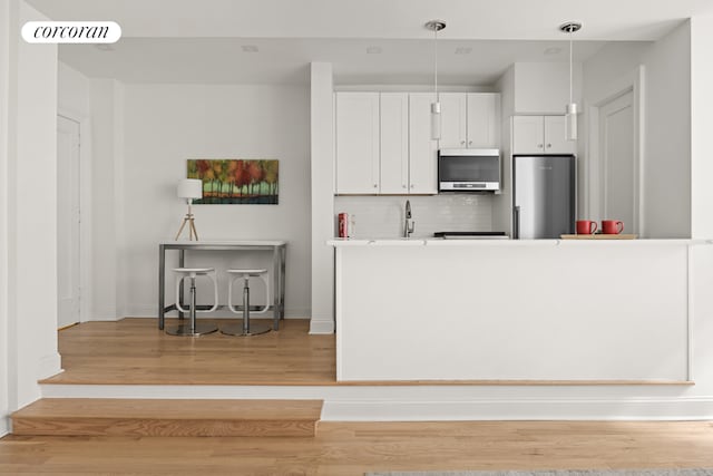 kitchen with white cabinetry, light hardwood / wood-style floors, backsplash, stainless steel refrigerator, and pendant lighting