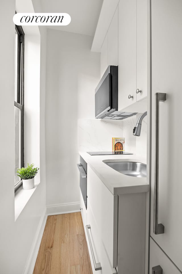 kitchen featuring white cabinets, light wood-style floors, baseboards, light countertops, and a sink