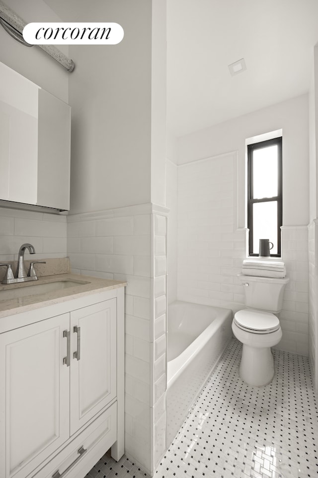 full bathroom with tile walls, a wainscoted wall, toilet, vanity, and a tub to relax in