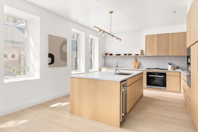 kitchen featuring a center island with sink, modern cabinets, light brown cabinets, a sink, and black oven