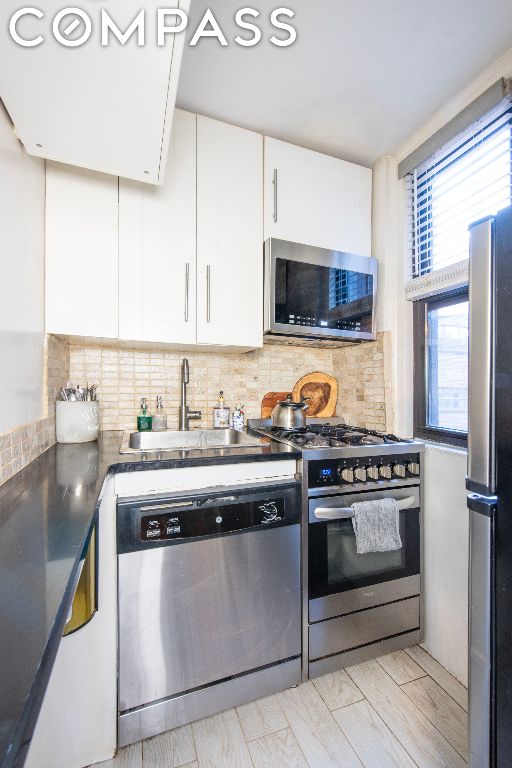 kitchen with backsplash, sink, stainless steel appliances, and white cabinetry