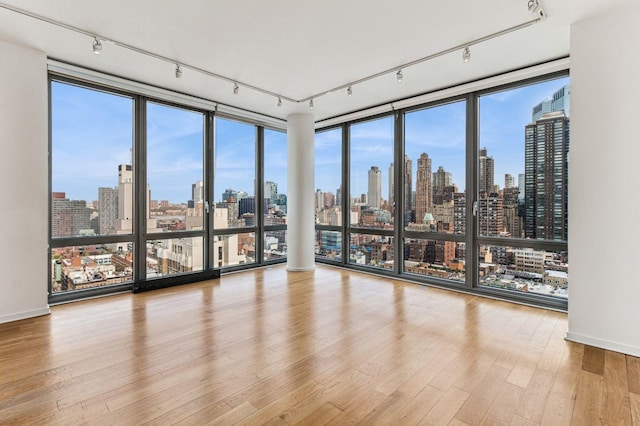 spare room with floor to ceiling windows, wood finished floors, rail lighting, and a city view