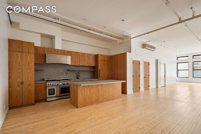 kitchen featuring a towering ceiling, range with two ovens, a kitchen island, an AC wall unit, and light wood-type flooring