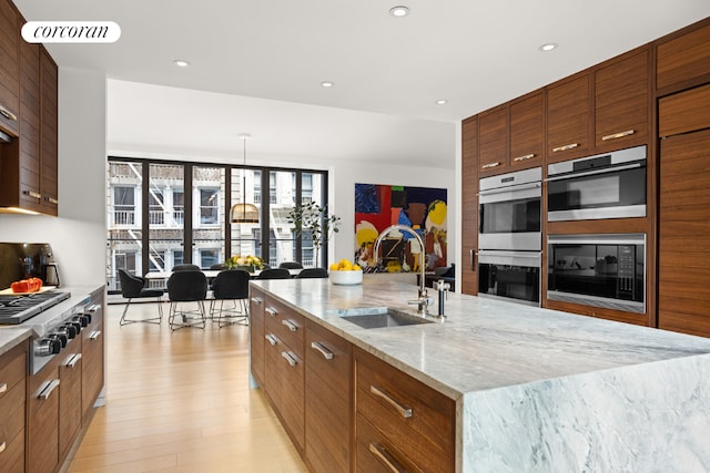 kitchen with a large island with sink, decorative light fixtures, stainless steel appliances, sink, and light hardwood / wood-style flooring