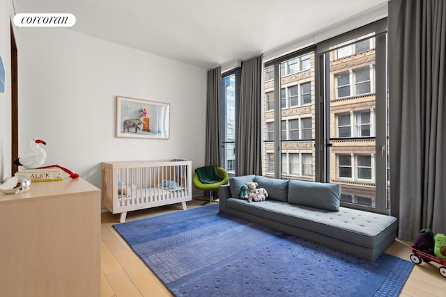 bedroom with a wall of windows, hardwood / wood-style flooring, and a crib