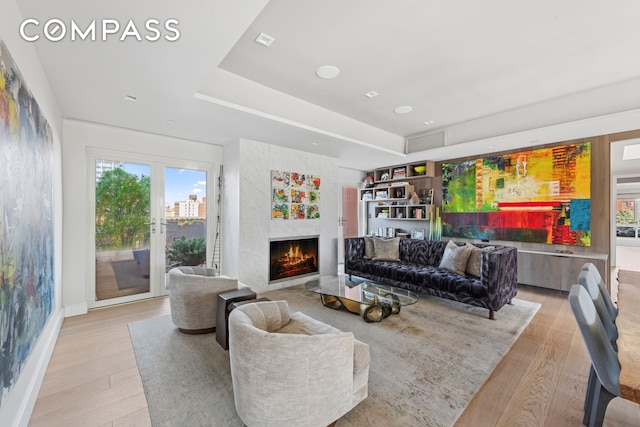 living area featuring light wood-style flooring, a premium fireplace, and a tray ceiling