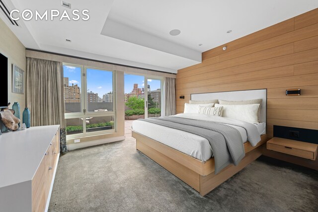 bedroom featuring a city view, access to exterior, wood walls, and carpet floors