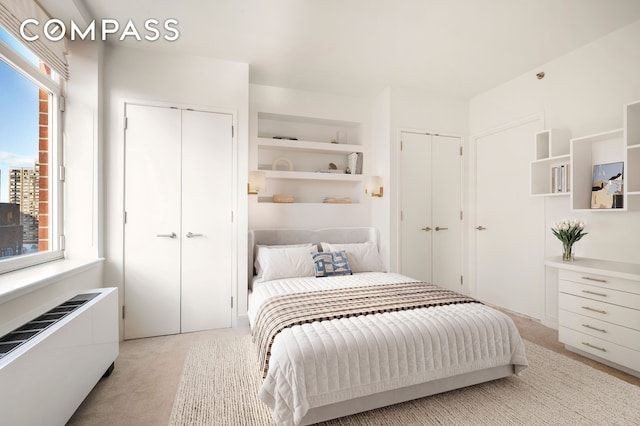 bedroom featuring multiple closets, radiator, and light colored carpet