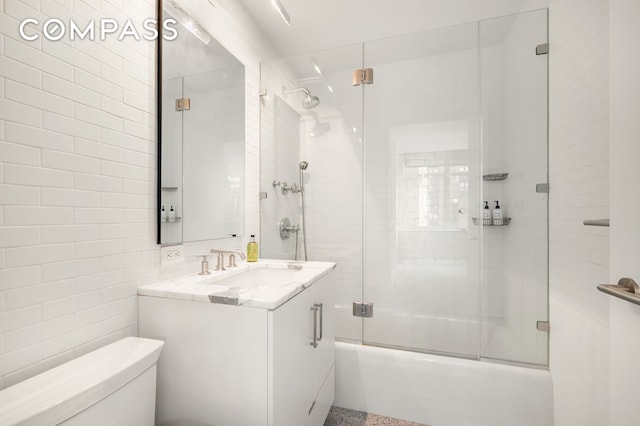 full bathroom featuring tile walls, toilet, vanity, and bath / shower combo with glass door