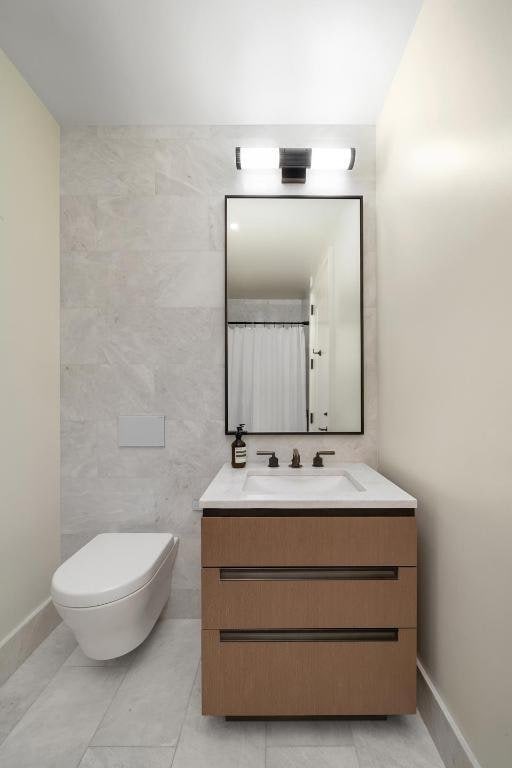 bathroom featuring vanity, tile walls, and toilet