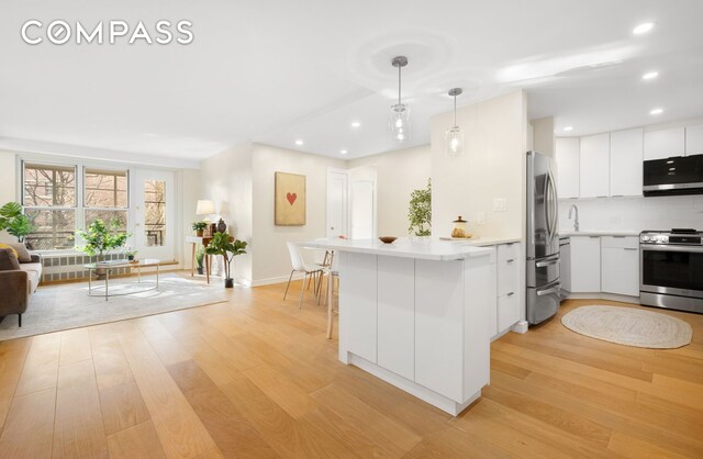 kitchen with white cabinetry, hanging light fixtures, stainless steel appliances, light hardwood / wood-style floors, and kitchen peninsula