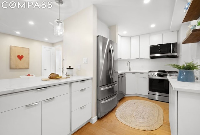 kitchen featuring hanging light fixtures, sink, stainless steel appliances, and white cabinetry