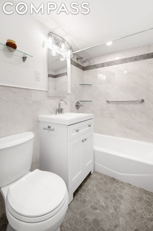 full bathroom with tile walls, toilet, vanity, and shower / washtub combination