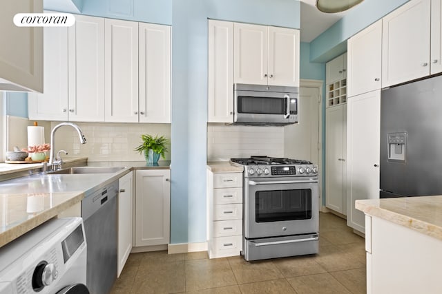 kitchen featuring appliances with stainless steel finishes, washer / dryer, white cabinetry, tasteful backsplash, and sink