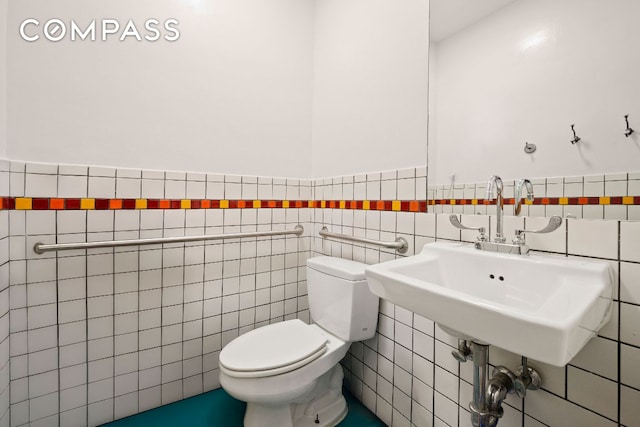 bathroom featuring toilet, tile walls, a sink, and wainscoting