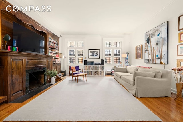 living area featuring wood finished floors, a fireplace with flush hearth, and crown molding