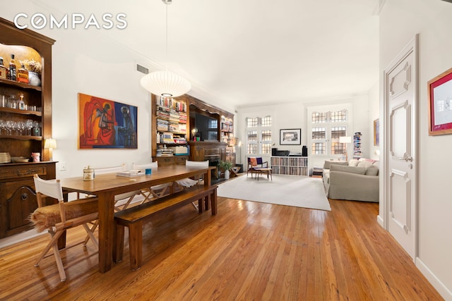 dining space with a fireplace, light wood-style flooring, visible vents, and built in shelves