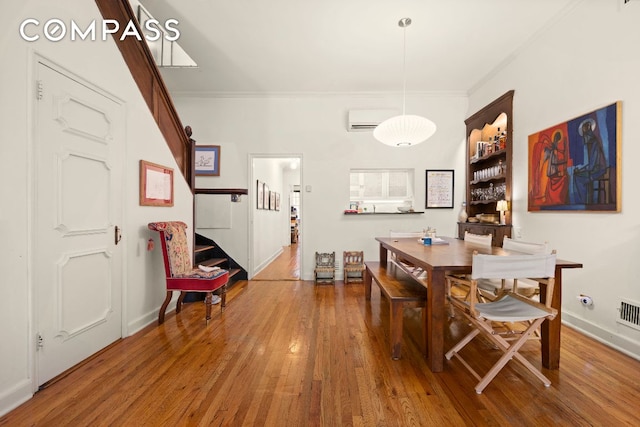 dining area featuring baseboards, a wall unit AC, wood finished floors, stairs, and crown molding