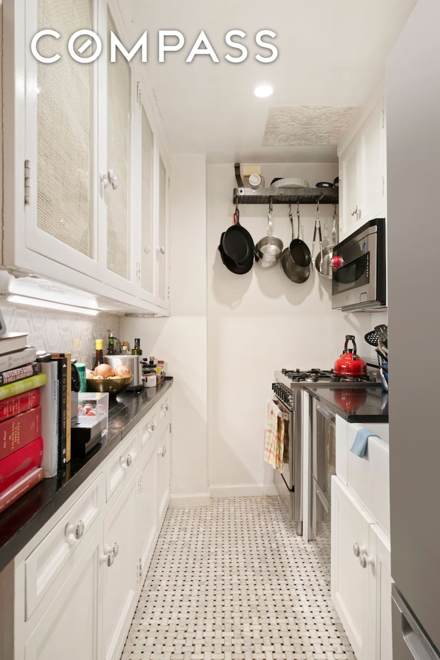 kitchen with dark countertops, white cabinetry, backsplash, baseboards, and appliances with stainless steel finishes
