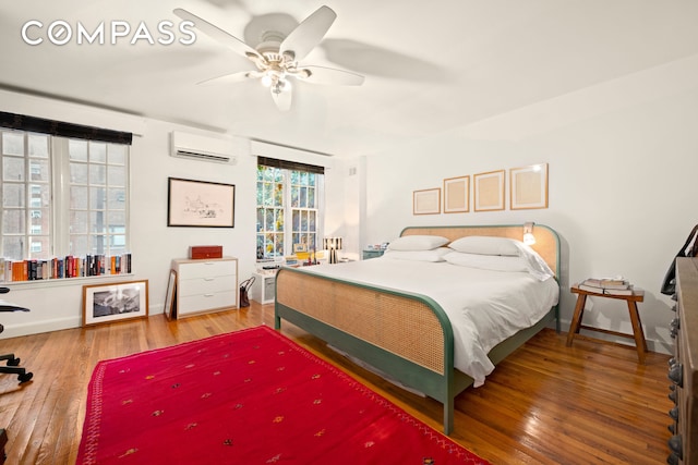 bedroom featuring a wall mounted air conditioner, wood-type flooring, baseboards, and a ceiling fan