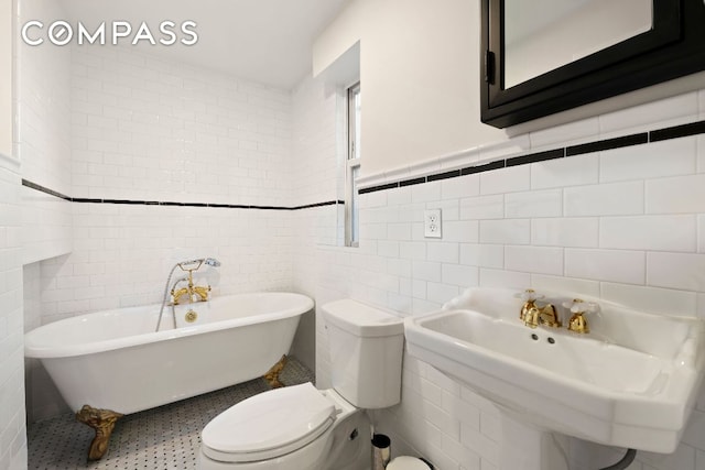 bathroom featuring toilet, a sink, tile walls, and a freestanding bath