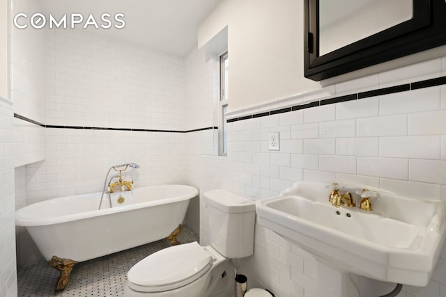 bathroom with tile walls, a sink, a freestanding bath, and toilet