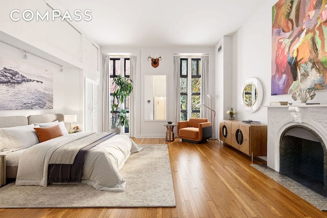 bedroom featuring light wood-type flooring, access to exterior, and a fireplace with flush hearth