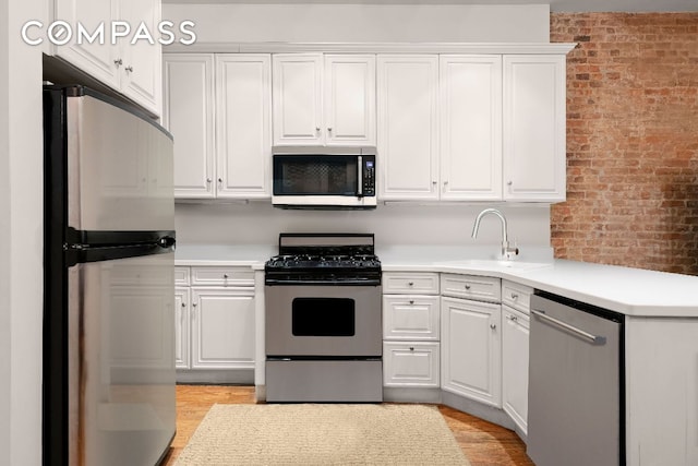 kitchen featuring stainless steel appliances, brick wall, a sink, white cabinetry, and light countertops