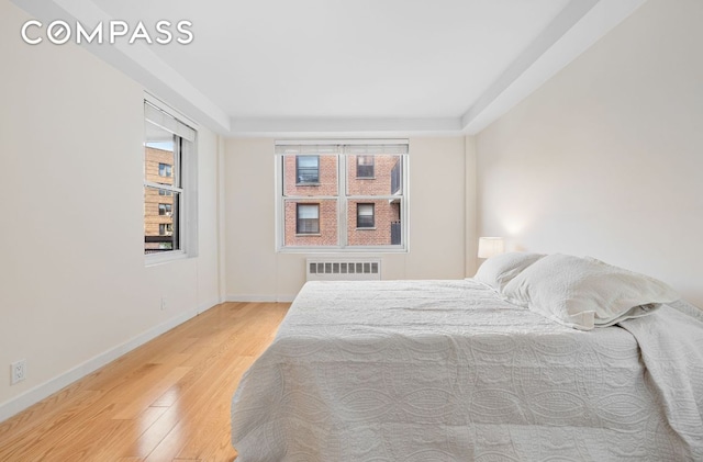 bedroom featuring radiator heating unit, hardwood / wood-style floors, and multiple windows